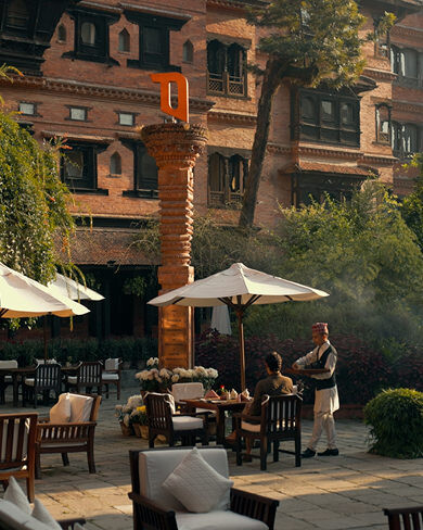 Waiter serving guests in the courtyard with carved wooden pillar and heritage buildings